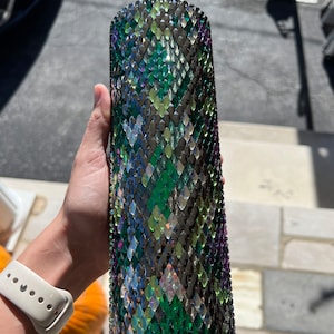 May include: A stainless steel tumbler with a green, black and purple snakeskin pattern covered in rhinestones.