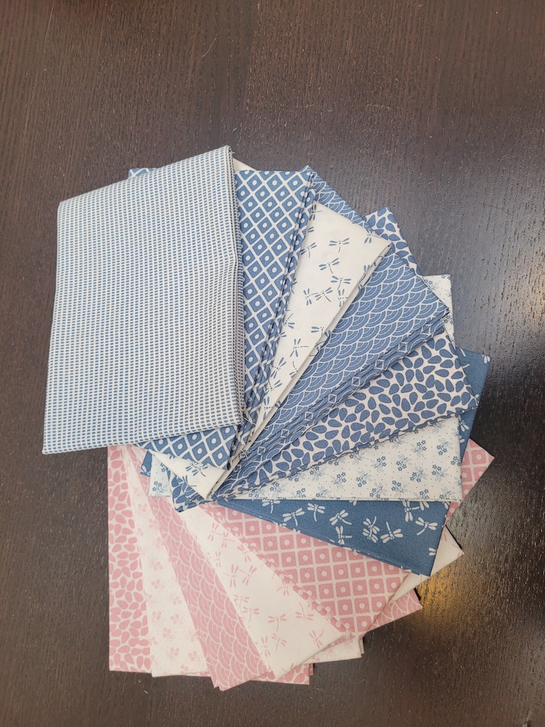 May include: A stack of 12 fabric squares in shades of blue and pink with various patterns, including geometric designs, dragonflies, and floral motifs.