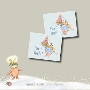 Könnte beinhalten: Zwei blaue Geschenkanhänger mit einem Comic-Dachs, der Geschenke trägt und den Text "Für Dich!" auf hellblauem Hintergrund. Ein brauner Bär mit einer Kerzenkrone ist im Vordergrund.