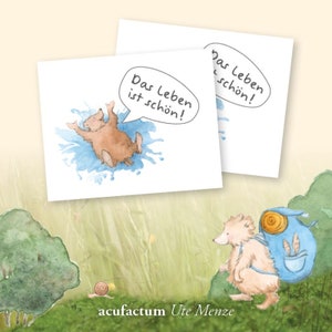 Peut inclure: Deux cartes illustrées avec un ours brun dans une flaque bleue et le texte "Das Leben ist schön!" qui signifie "La vie est belle!" en allemand. Les cartes sont sur un fond vert herbeux avec un escargot brun et un ours brun avec un sac à dos bleu.