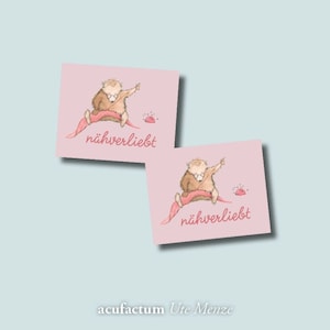 Könnte beinhalten: Zwei rosa Karten mit einem niedlichen Comic-Igel, der mit Nadel und Faden näht. Die Karten tragen den Text "nähverliebt", was im Deutschen "Nähliebhaber" bedeutet.