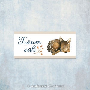 May include: A light brown fawn with white spots sleeps on a white background with the text "Träum süß" and a small brown branch with orange leaves.