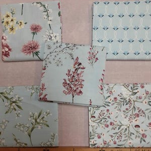 Puede incluir: Cinco cuadrados de tela con patrones florales sobre un fondo azul claro. Los patrones incluyen pequeñas flores blancas, flores rosas y un patrón geométrico.