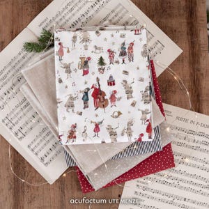Op de afbeelding: Een stapel gevouwen stoffen, waaronder een wit textiel met een herhalend patroon van geïllustreerde figuren die muziekinstrumenten bespelen, een effen beige stuk, een marineblauw en wit gestreept stuk, een grijs gestippeld stuk en een rood gestippeld stuk.
