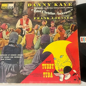 May include: Vintage vinyl record album cover for "Danny Kaye Sings Selections from Hans Christian Andersen." The cover features a colorful illustration of Danny Kaye with children, and a cartoon character. The record is a Decca Records long play.