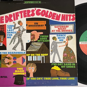 May include: A vintage vinyl record album cover featuring The Drifters' Golden Hits. The cover is black with a colorful design featuring the band's name and a list of their hit songs, including "Under the Boardwalk", "Save the Last Dance for Me", "On Broadway", "Saturday Night at the Movies", "There Goes My Baby", "Dance With Me", "Up on the Roof", "This Magic Moment", "I've Got Sand in My Shoes", and "True Love, True Love".