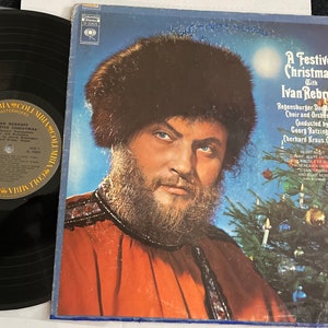 May include: A vintage vinyl record album titled "A Festive Christmas with Ivan Rebroff." The album cover features a portrait of a man in a fur hat and red clothing, with a Christmas tree in the background. The record itself is black.