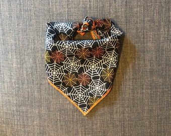 Könnte beinhalten: Schwarzes Bandana mit einem weißen und orangefarbenen Spinnennetz-Muster. Das Bandana hat einen gelben Saum.