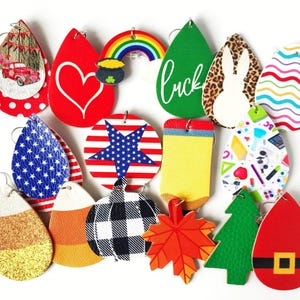 K&ouml;nnte beinhalten: Eine Sammlung farbenfroher, thematischer Ohrringe. Designs umfassen einen roten Truck, ein Herz, einen Regenbogen, ein gr&uuml;nes Blatt mit dem Text "luck", ein Kaninchen, die amerikanische Flagge, Zuckermais, einen K&uuml;rbis, ein Ahornblatt und einen Weihnachtsbaum.