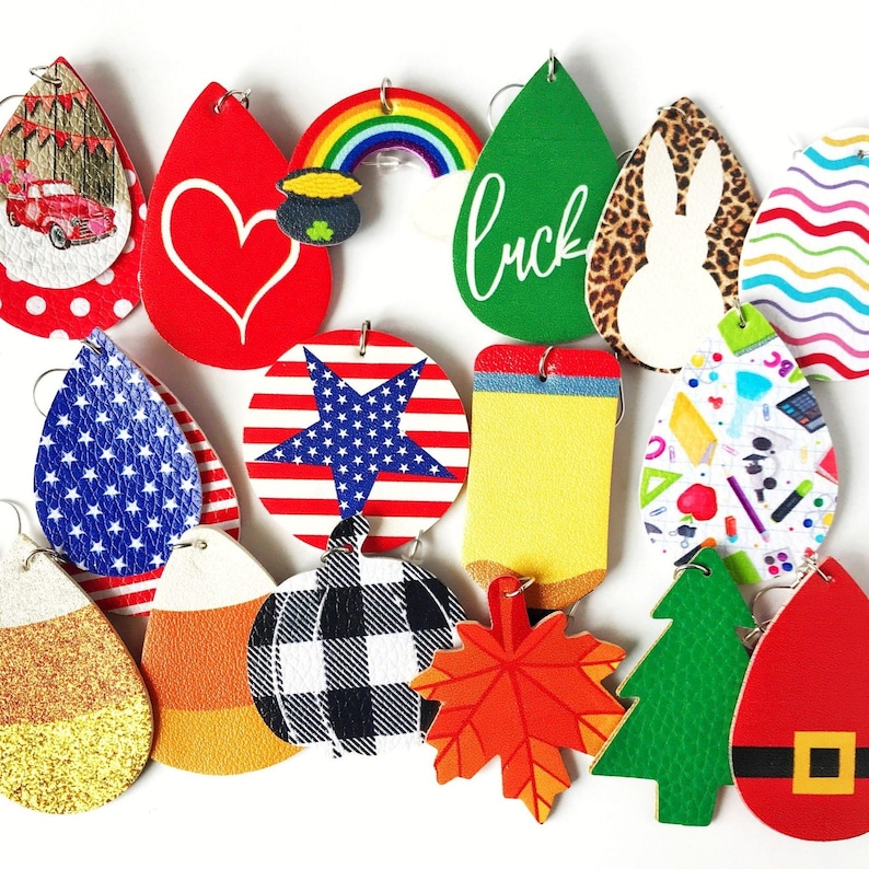 K&ouml;nnte beinhalten: Eine Sammlung farbenfroher, thematischer Ohrringe. Designs umfassen einen roten Truck, ein Herz, einen Regenbogen, ein gr&uuml;nes Blatt mit dem Text "luck", ein Kaninchen, die amerikanische Flagge, Zuckermais, einen K&uuml;rbis, ein Ahornblatt und einen Weihnachtsbaum.