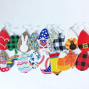 K&ouml;nnte beinhalten: Eine Sammlung farbenfroher, thematischer Ohrh&auml;nger. Zu den Designs geh&ouml;ren ein rotes Herz, ein gr&uuml;nes Kleeblatt, ein Hase, ein Zwerg und ein Baseball. Weitere Ohrringe zeigen einen Truthahn, ein Herbstblatt und ein rot-schwarzes Karomuster. Jeder Ohrring hat einen silbernen Haken.