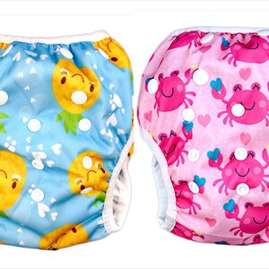 May include: Two reusable swim diapers, one with a blue pineapple print and the other with a pink crab print. Both diapers have white snaps.