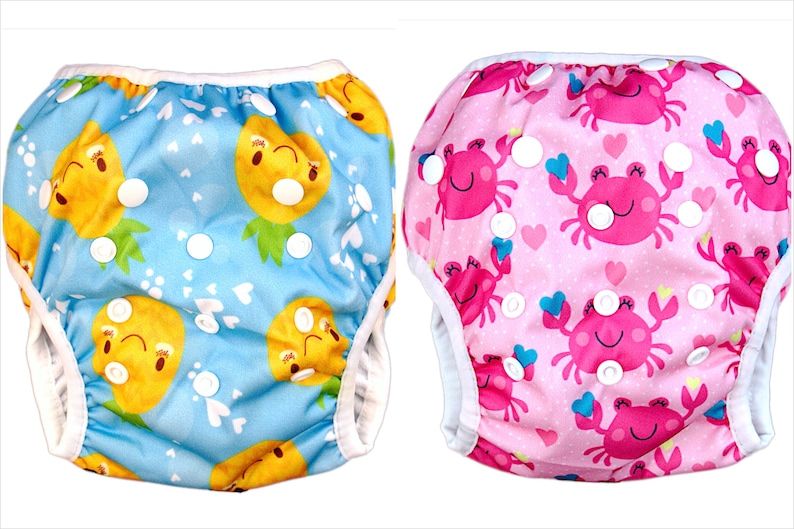 May include: Two reusable swim diapers, one with a blue pineapple print and the other with a pink crab print. Both diapers have white snaps.