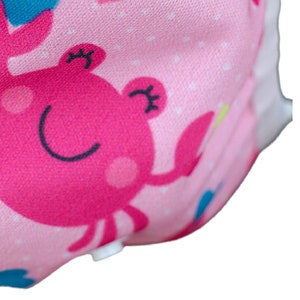 May include: Pink cloth diaper with a white snap closure and a pink and blue crab print.