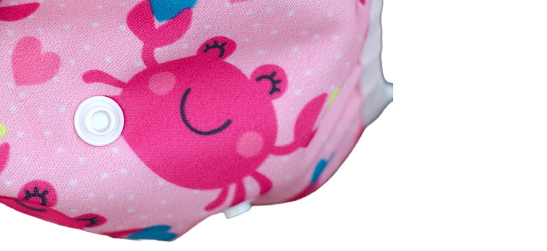 May include: Pink cloth diaper with a white snap closure and a pink and blue crab print.