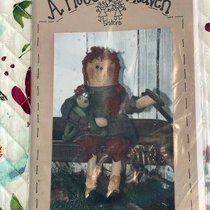 May include: A Piece of Heaven Sisters pattern for a rag doll named Nancy Ann, 41 inches tall. The pattern shows a red-haired doll with a frog friend sitting on a bench.