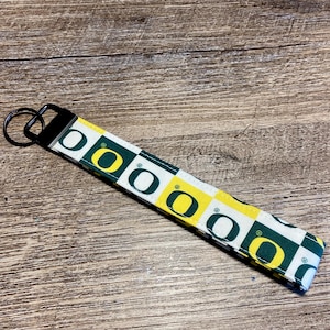 May include: A white, yellow, and green key chain with the University of Oregon logo repeated on a checkered pattern.