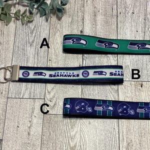 May include: Three keychains with Seattle Seahawks designs. One is green with a repeating logo, another is navy blue with the text "Seattle Seahawks", and the third is navy blue with repeating helmets and logos. All have silver key rings.
