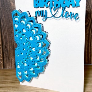 Puede incluir: Una tarjeta de papel azul y blanco con el texto "Happy 28th Birthday my love" y un diseño de mandala de papel azul.