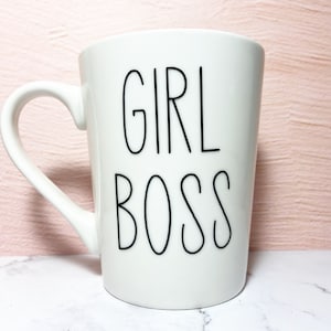 Op de afbeelding: Witte keramische mok met een zwart handvat en de tekst "GIRL BOSS" gedrukt op de voorkant.