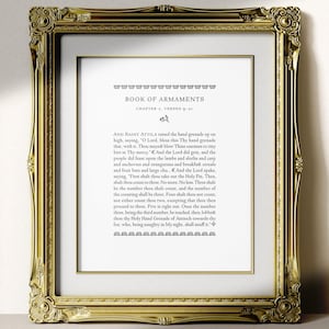 May include: A framed print with an elaborate gold frame. The print displays text from the "Book of Armaments" in a traditional serif typeface. The text is set against a white backdrop, and the frame adds a touch of sophistication.
