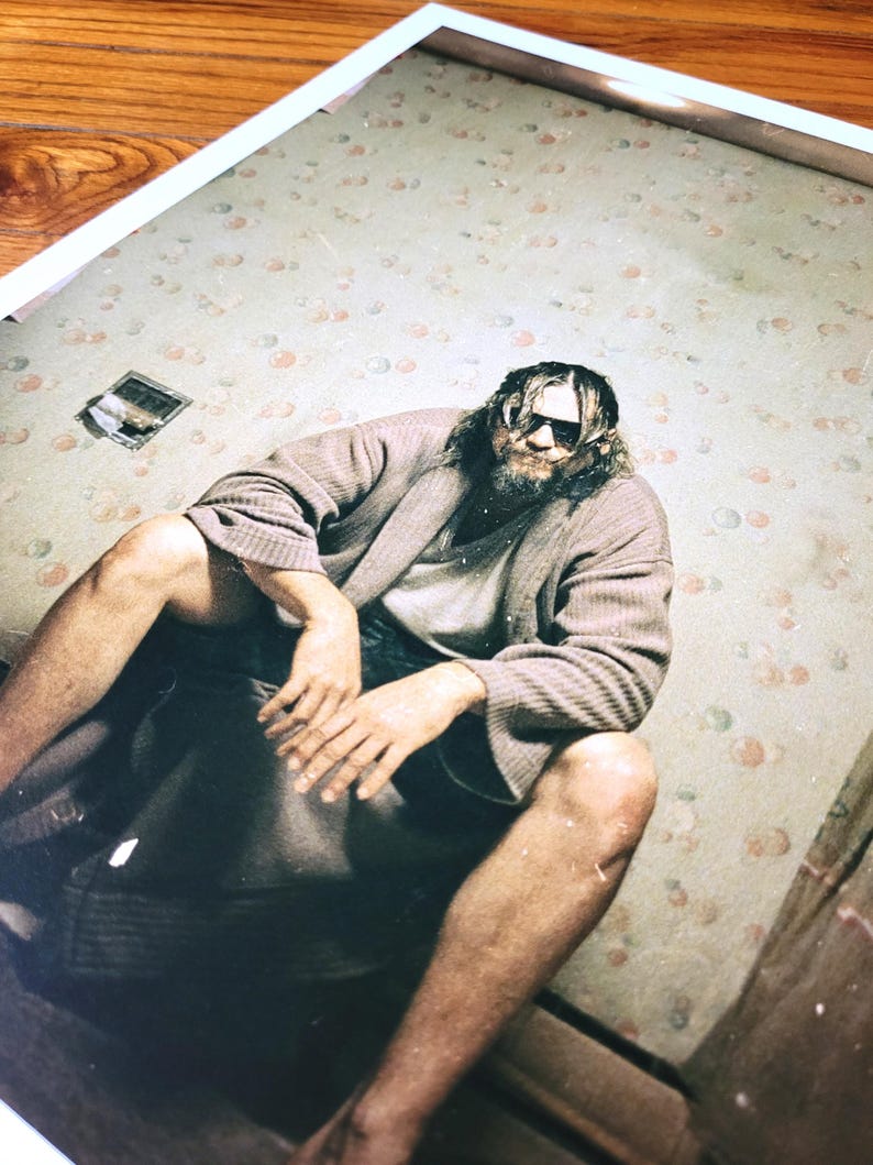K&ouml;nnte beinhalten: Ein Mann in einem braunen Bademantel und Sonnenbrille sitzt auf einem Bett mit einem floral gemusterten Kopfteil. Das Zimmer hat eine Tapete mit floralem Muster.