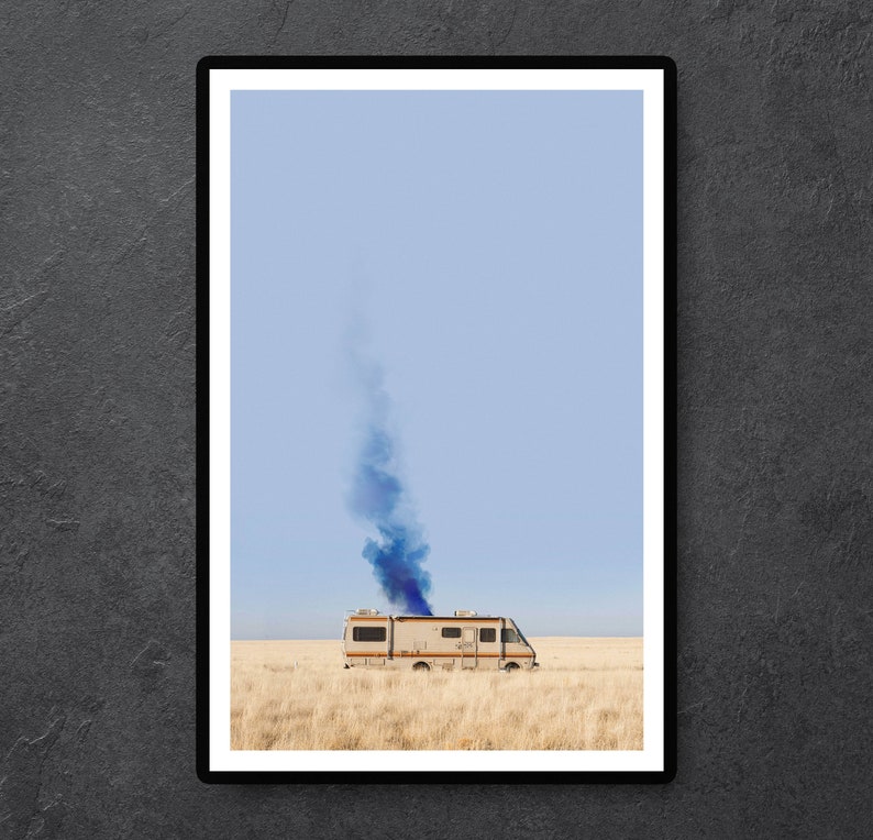 May include: A white RV with a blue smoke plume coming from the top, driving across a dry, brown field under a light blue sky.