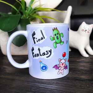 Könnte beinhalten: Weiße Keramiktasse mit blauem Hintergrund und bunten Comicfiguren aus der Videospielserie Final Fantasy. Die Tasse trägt die Aufschrift "Final Fantasy" in schwarzer Schrift.