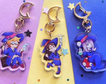 Puede incluir: Tres llaveros de acrílico coloridos con personajes de anime con sombreros de bruja. Los personajes sostienen varitas mágicas, una botella de poción y un libro. Cada llavero tiene un cierre de metal dorado en forma de media luna.