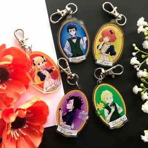 May include: Five colorful oval-shaped keychains with cartoon characters. Each keychain features a different character with a name printed below. The characters are a girl with blonde hair, a boy with brown hair, a girl with red hair, a boy with blonde hair, and a girl with black hair.