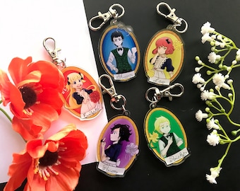 May include: Five colourful oval-shaped keychains with cartoon characters. Each keychain features a different character with a name printed below. The characters are a girl with blonde hair, a boy with brown hair, a girl with red hair, a boy with blonde hair, and a girl with black hair.