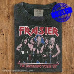 May include: A charcoal grey crew neck t-shirt featuring a graphic print of four people in black leather-style clothing. The text reads FRASIER above the figures and IN THE MIX TOUR '97 below. The shirt has a Comfort Colors brand neck label.