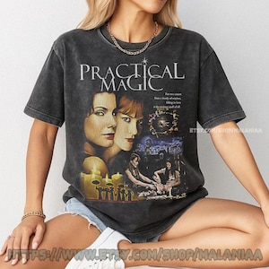 May include: Dark gray t-shirt featuring the movie title "Practical Magic" with images of the film's stars and scenes. The shirt has a vintage, worn look, and the text "ETSY.COM/SHOP/MALANIAA" is visible.