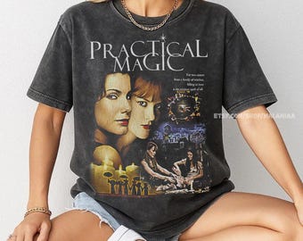 May include: Dark gray t-shirt featuring the movie title "Practical Magic" with images of the film's stars and scenes. The shirt has a vintage, worn look, and the text "ETSY.COM/SHOP/MALANIAA" is visible.