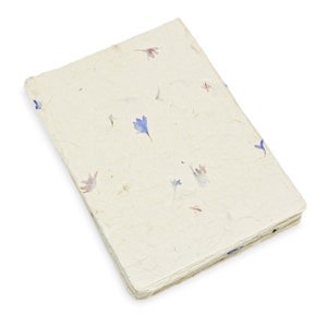 May include: A rectangular notebook with a textured, off-white cover made of handmade paper. The cover is embedded with small, scattered dried flower petals in shades of blue, pink, and purple, featuring a deckled edge and visible paper fibers.