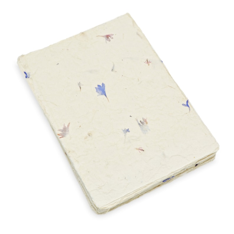 May include: A rectangular notebook with a textured, off-white cover made of handmade paper. The cover is embedded with small, scattered dried flower petals in shades of blue, pink, and purple, featuring a deckled edge and visible paper fibers.