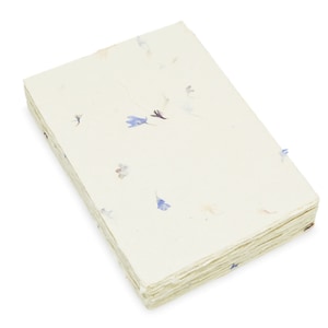 May include: A rectangular stack of off-white handmade paper sheets with a deckled edge. The paper features embedded small, dried blue and purple flower petals scattered across the surface, creating a textured and organic appearance throughout.