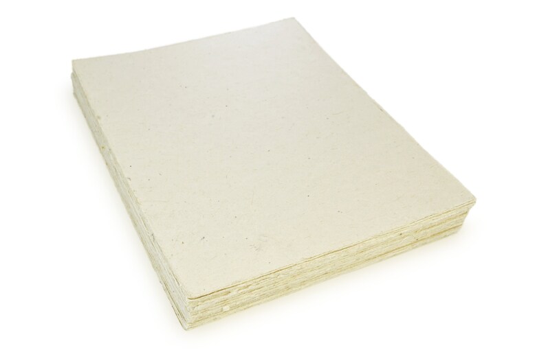 Puede incluir: Una pila de hojas de papel de color blanquecino, probablemente hechas a mano, con una textura rugosa. El papel es ligeramente transl&uacute;cido y tiene un aspecto natural y r&uacute;stico.
