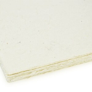 Puede incluir: Una pila de hojas de papel hecho a mano de color blanco roto con una superficie rugosa y texturizada.