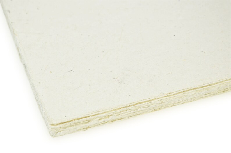 Puede incluir: Una pila de hojas de papel hecho a mano de color blanco roto con una superficie rugosa y texturizada.