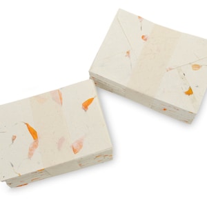 May include: A stack of white envelopes with orange flower petals embedded in the paper. The envelopes are folded and stacked on top of each other.