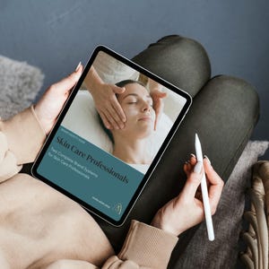 May include: A tablet displaying a skincare guide titled "Skin Care Professionals." The image on the tablet shows a person receiving a facial treatment. A white stylus is held in the hand. The person is sitting on a chair.