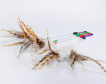 May include: A set of cat teaser wands featuring long, thin metal rods with colorful plastic handles in black, green, red, blue, and white. Each wand is topped with a cluster of natural brown, tan, and white striped feathers for interactive play.