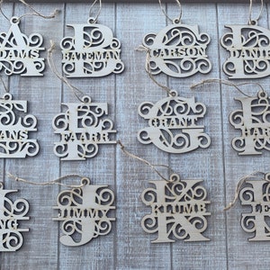 May include: Twelve wooden ornaments with a decorative, intricate design. Each ornament features a large letter with a name written below it. The names are Adams, Bateman, Carson, Daniel, Evans, Farr, Grant, Harvey, Irving, Jimmy, Klumbe, and Leon.