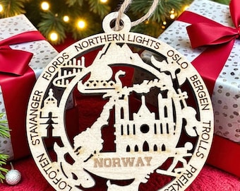May include: A wooden Christmas ornament with a Norway theme. The ornament is circular with cut-out designs of landmarks and the word "NORWAY". The ornament has a natural wood color and is suspended by a twine loop. The ornament is surrounded by gift boxes with red bows.