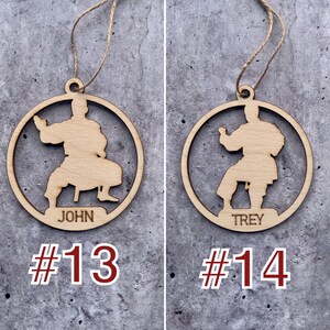 May include: Two wooden ornaments featuring a silhouette of a person in a karate pose. The ornament on the left reads "JOHN #13" and the ornament on the right reads "TREY #14".