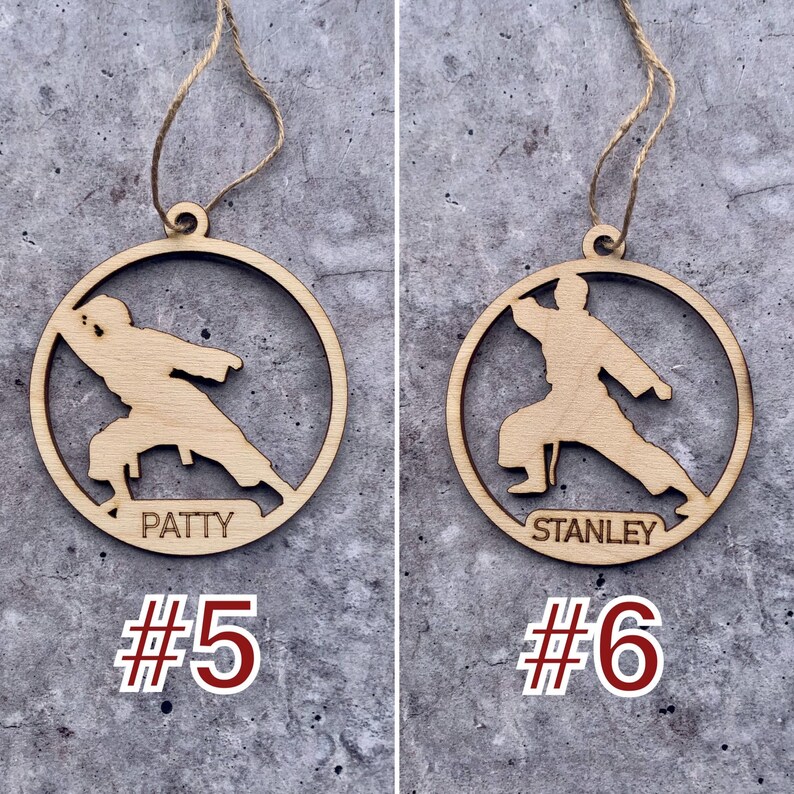 May include: Two wooden Christmas decorations shaped like a karate person with the names "PATTY" and "STANLEY" engraved on them. The decorations are hanging from a string and are numbered #5 and #6.