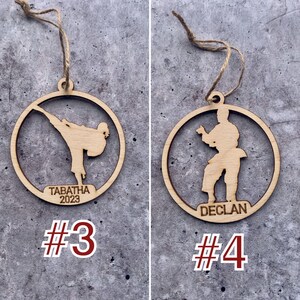May include: Two wooden Christmas decorations featuring a silhouette of a person in a karate pose. The ornament on the left has the name "Tabatha 2023" and the number "#3" below it. The ornament on the right has the name "Declan" and the number "#4" below it.