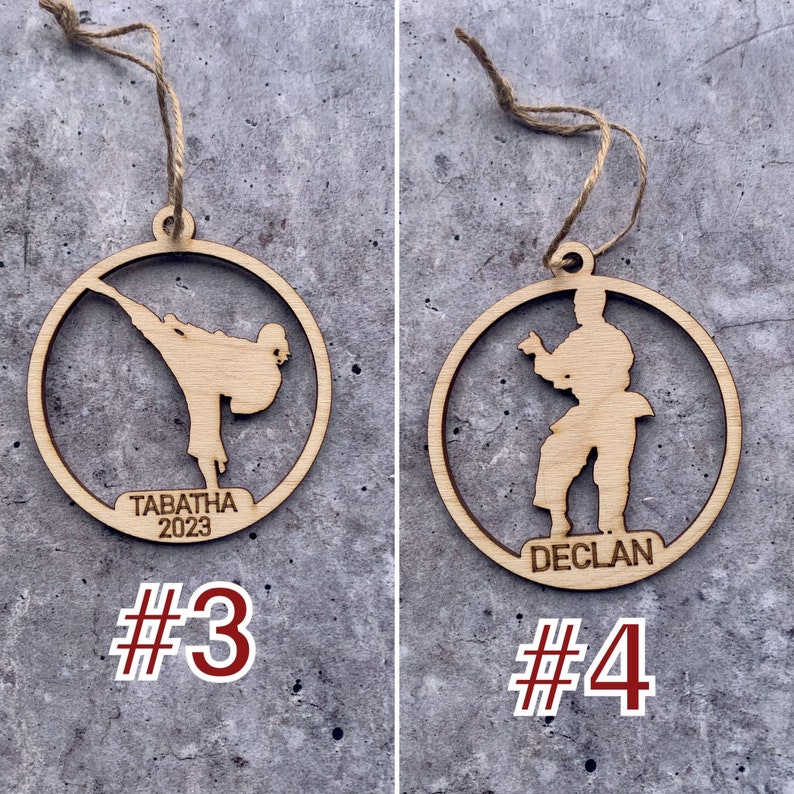 May include: Two wooden Christmas decorations featuring a silhouette of a person in a karate pose. The ornament on the left has the name "Tabatha 2023" and the number "#3" below it. The ornament on the right has the name "Declan" and the number "#4" below it.