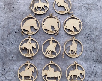 Puede incluir: Doce adornos de madera con forma de caballo, cada uno con un nombre diferente escrito en él. Los adornos son todos del mismo estilo, con una silueta de caballo y un jinete. Los nombres en los adornos son: Tally, Bella, Horsey, Zoe, Candice, Misty, Lenny, Matthew, Steve y Wendy.